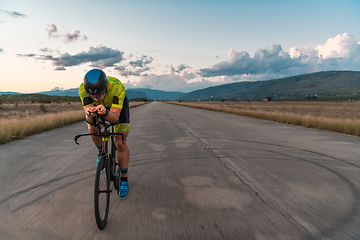 Image showing Triathlete riding his bicycle during sunset, preparing for a marathon. The warm colors of the sky provide a beautiful backdrop for his determined and focused effort.