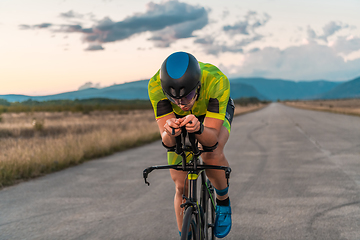 Image showing Triathlete riding his bicycle during sunset, preparing for a marathon. The warm colors of the sky provide a beautiful backdrop for his determined and focused effort.