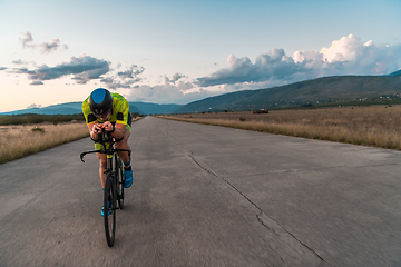 Image showing Triathlete riding his bicycle during sunset, preparing for a marathon. The warm colors of the sky provide a beautiful backdrop for his determined and focused effort.