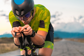 Image showing Close up photo of triathlete riding his bicycle during sunset, preparing for a marathon. The warm colors of the sky provide a beautiful backdrop for his determined and focused effort.