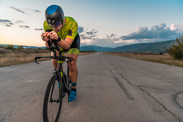 Image showing Triathlete riding his bicycle during sunset, preparing for a marathon. The warm colors of the sky provide a beautiful backdrop for his determined and focused effort.