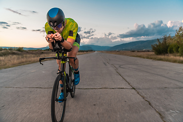 Image showing Triathlete riding his bicycle during sunset, preparing for a marathon. The warm colors of the sky provide a beautiful backdrop for his determined and focused effort.