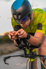 Image showing Close up photo of triathlete riding his bicycle during sunset, preparing for a marathon. The warm colors of the sky provide a beautiful backdrop for his determined and focused effort.