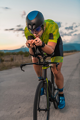 Image showing Triathlete riding his bicycle during sunset, preparing for a marathon. The warm colors of the sky provide a beautiful backdrop for his determined and focused effort.