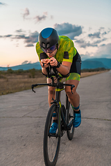 Image showing Triathlete riding his bicycle during sunset, preparing for a marathon. The warm colors of the sky provide a beautiful backdrop for his determined and focused effort.