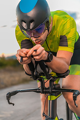 Image showing Close up photo of triathlete riding his bicycle during sunset, preparing for a marathon. The warm colors of the sky provide a beautiful backdrop for his determined and focused effort.