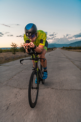 Image showing Triathlete riding his bicycle during sunset, preparing for a marathon. The warm colors of the sky provide a beautiful backdrop for his determined and focused effort.