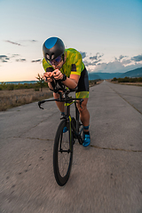 Image showing Triathlete riding his bicycle during sunset, preparing for a marathon. The warm colors of the sky provide a beautiful backdrop for his determined and focused effort.