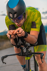 Image showing Triathlete riding his bicycle during sunset, preparing for a marathon. The warm colors of the sky provide a beautiful backdrop for his determined and focused effort.