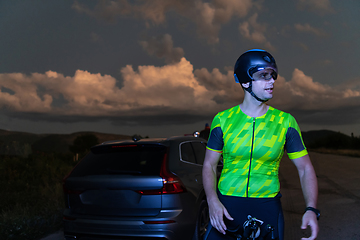 Image showing A triathlete resting on the road after a tough bike ride in the dark night, leaning on his bike in complete exhaustion