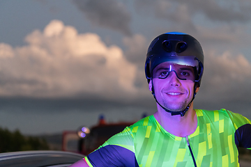 Image showing A triathlete resting on the road after a tough bike ride in the dark night, leaning on his bike in complete exhaustion
