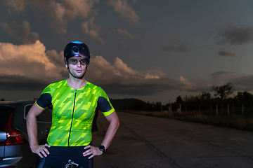 Image showing A triathlete resting on the road after a tough bike ride in the dark night, leaning on his bike in complete exhaustion