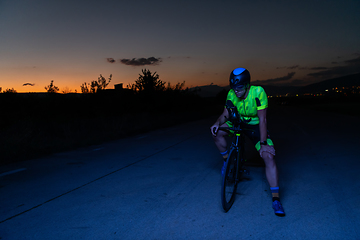 Image showing A triathlete resting on the road after a tough bike ride in the dark night, leaning on his bike in complete exhaustion