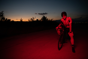 Image showing A triathlete resting on the road after a tough bike ride in the dark night, leaning on his bike in complete exhaustion