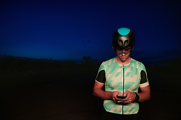 Image showing A triathlete using a smartphone while taking a break from a hard night's cycling training