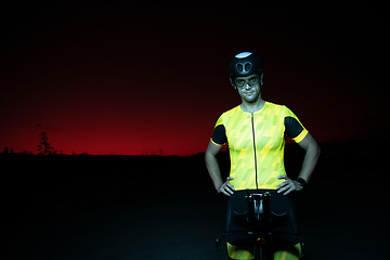 Image showing A triathlete resting on the road after a tough bike ride in the dark night, leaning on his bike in complete exhaustion