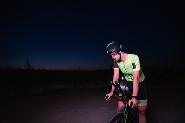 Image showing A triathlete resting on the road after a tough bike ride in the dark night, leaning on his bike in complete exhaustion