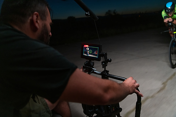 Image showing A videographer recording a triathlete riding his bike preparing for an upcoming marathon.Athlete's physical endurance and the dedication required to succeed in the sport.