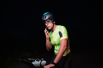 Image showing A triathlete using a smartphone while taking a break from a hard night's cycling training