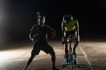 Image showing Behind the scenes. Professional videographer on a night shoot with a triathlete riding a bicycle for video recording purposes