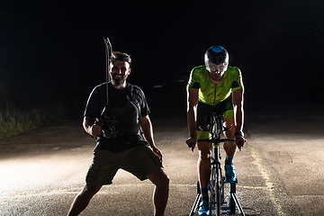 Image showing Behind the scenes. Professional videographer on a night shoot with a triathlete riding a bicycle for video recording purposes