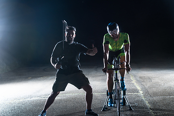 Image showing Behind the scenes. Professional videographer on a night shoot with a triathlete riding a bicycle for video recording purposes