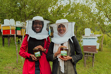 Image showing Portrait of an Arab investors holding a jar of honey in their hands while standing in front of a large honey farm. The concept of investing in small businesses