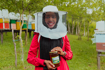 Image showing Portrait of a Muslim investitor in the beekeeping department of a honey farm holding a jar of honey in her hand