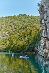 Image showing A group of friends enjoying having fun and kayaking while exploring the calm river, surrounding forest and large natural river canyons