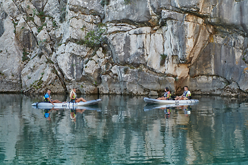 Image showing A group of friends enjoying having fun and kayaking while exploring the calm river, surrounding forest and large natural river canyons