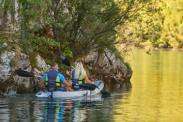 Image showing A young couple enjoying an idyllic kayak ride in the middle of a beautiful river surrounded by forest greenery