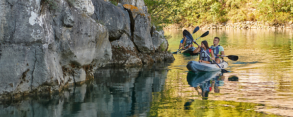 Image showing A group of friends enjoying having fun and kayaking while exploring the calm river, surrounding forest and large natural river canyons