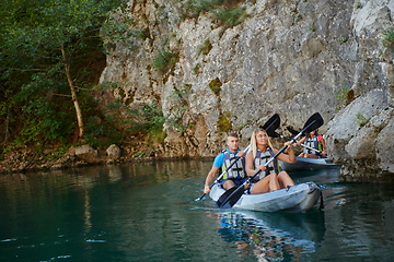 Image showing A group of friends enjoying having fun and kayaking while exploring the calm river, surrounding forest and large natural river canyons