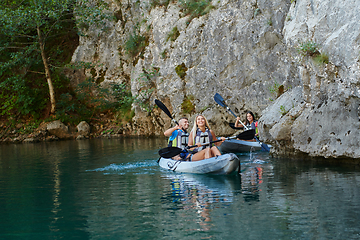 Image showing A group of friends enjoying having fun and kayaking while exploring the calm river, surrounding forest and large natural river canyons