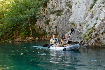 Image showing A young couple enjoying an idyllic kayak ride in the middle of a beautiful river surrounded by forest greenery