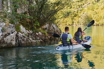 Image showing A young couple enjoying an idyllic kayak ride in the middle of a beautiful river surrounded by forest greenery