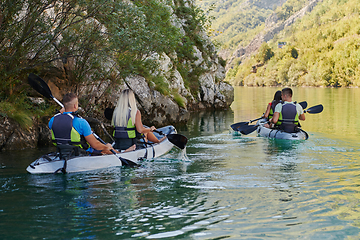 Image showing A group of friends enjoying having fun and kayaking while exploring the calm river, surrounding forest and large natural river canyons