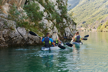 Image showing A group of friends enjoying having fun and kayaking while exploring the calm river, surrounding forest and large natural river canyons