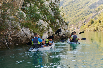 Image showing A group of friends enjoying having fun and kayaking while exploring the calm river, surrounding forest and large natural river canyons