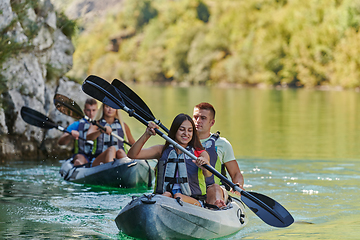 Image showing A group of friends enjoying having fun and kayaking while exploring the calm river, surrounding forest and large natural river canyons