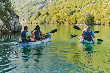 Image showing A group of friends enjoying having fun and kayaking while exploring the calm river, surrounding forest and large natural river canyons