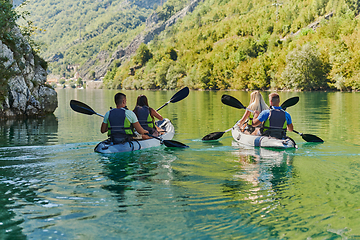 Image showing A group of friends enjoying having fun and kayaking while exploring the calm river, surrounding forest and large natural river canyons