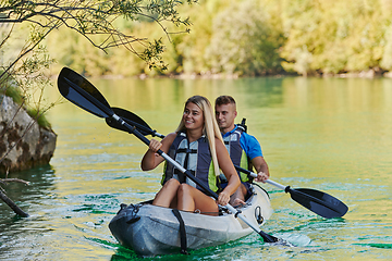 Image showing A young couple enjoying an idyllic kayak ride in the middle of a beautiful river surrounded by forest greenery