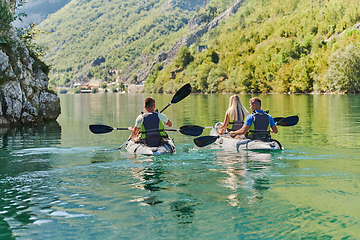 Image showing A group of friends enjoying having fun and kayaking while exploring the calm river, surrounding forest and large natural river canyons