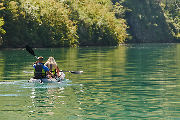 Image showing A young couple enjoying an idyllic kayak ride in the middle of a beautiful river surrounded by forest greenery