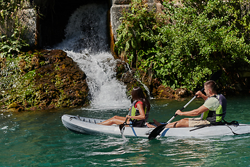 Image showing A young couple enjoying an idyllic kayak ride in the middle of a beautiful river surrounded by forest greenery