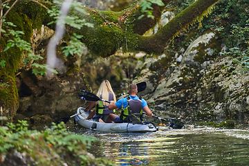 Image showing A young couple enjoying an idyllic kayak ride in the middle of a beautiful river surrounded by forest greenery