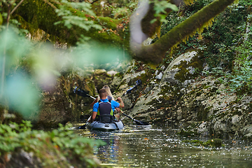 Image showing A young couple enjoying an idyllic kayak ride in the middle of a beautiful river surrounded by forest greenery