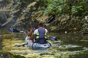 Image showing A young couple enjoying an idyllic kayak ride in the middle of a beautiful river surrounded by forest greenery