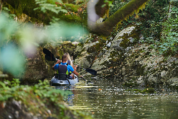 Image showing A young couple enjoying an idyllic kayak ride in the middle of a beautiful river surrounded by forest greenery